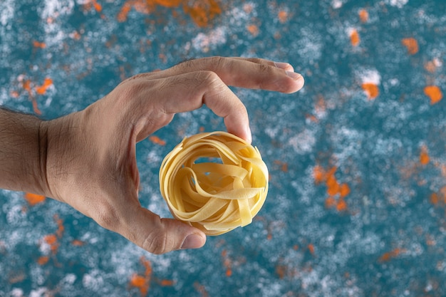 Männliche Hand, die Tagliatelle Nest hält.