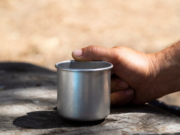 Männliche Hand, die Weinlesemetallbecher am sonnigen Tag hält