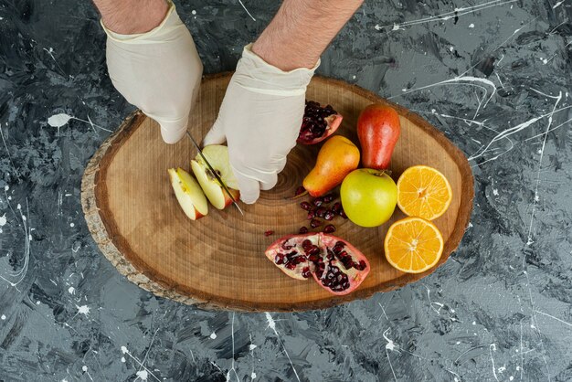 Männliche Hand in Handschuhen, die frischen Apfel auf Marmortisch schneiden.