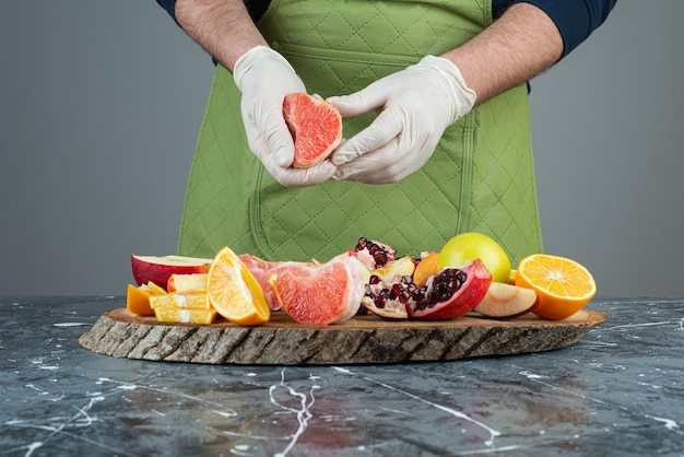 Männliche Hand in Handschuhen, die saftige Grapefruit auf Marmortisch schneiden.