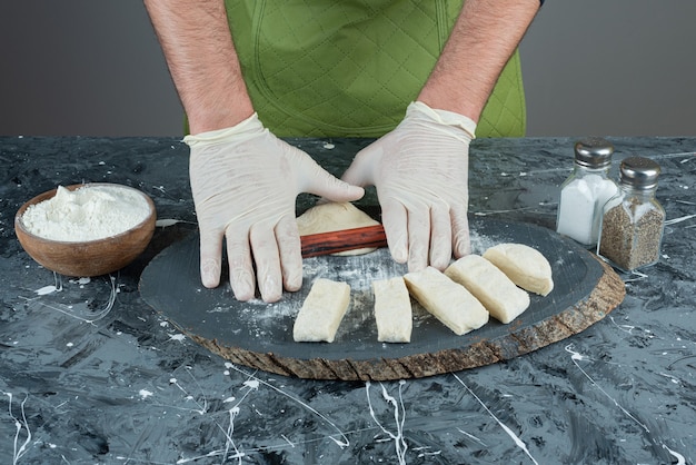 Männliche Hand in Handschuhen, die Teig auf Marmortisch machen.