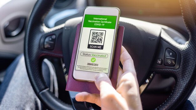 Männliche Hand mit Reisepass und Smartphone mit internationalem Impfzertifikat COVID-19 QR-Code in einem Auto