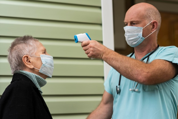 Männliche Krankenschwester, die die Temperatur der älteren Frau mit Thermometer prüft