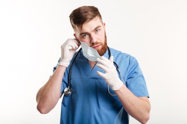 Männliche medizinische Assistentin mit Stethoskop, das seine Maske abnimmt