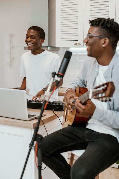 Männliche Smiley-Musiker zu Hause, die Gitarre und elektrisches Keyboard spielen