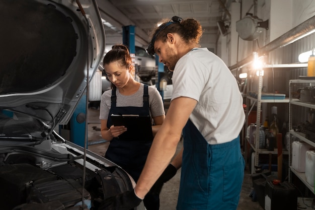 Kostenloses Foto männliche und weibliche mechaniker, die in der werkstatt an einem auto arbeiten