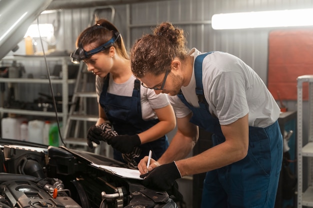 Männliche und weibliche Mechaniker, die in der Werkstatt an einem Auto arbeiten
