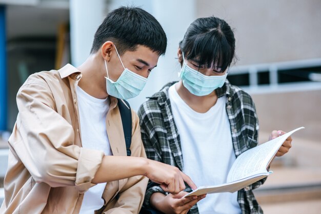 Männliche und weibliche Studenten, die Masken tragen, sitzen und lesen Bücher auf der Treppe