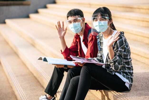 Männliche und weibliche Studenten, die Masken tragen, sitzen und lesen Bücher auf der Treppe