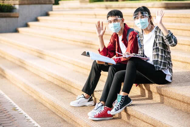 Männliche und weibliche Studenten, die Masken tragen, sitzen und lesen Bücher auf der Treppe