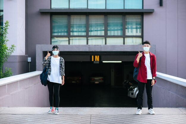 Männliche und weibliche Studenten tragen Masken und stehen vor der Universität.