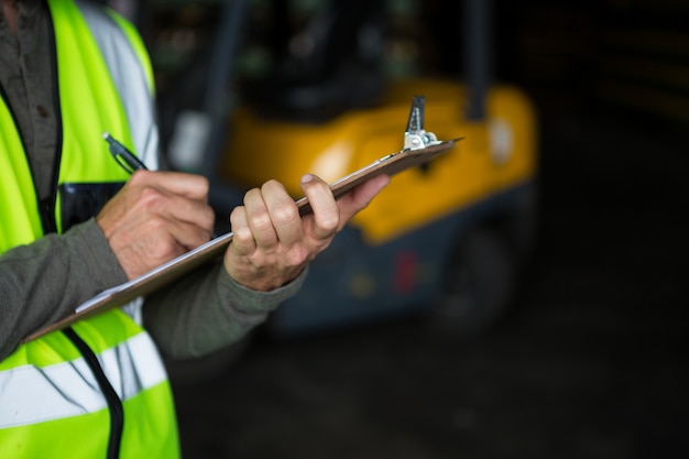 Männlicher Arbeiter, der auf Zwischenablage schreibt