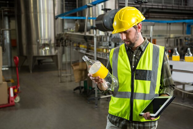 Männlicher Arbeiter, der Flaschen in der Saftfabrik inspiziert