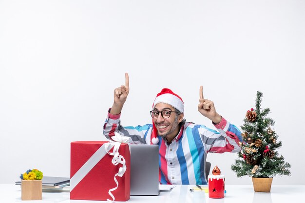 Männlicher Arbeiter der Vorderansicht, der an seinem Arbeitsplatz sitzt und lächelt, Geschäftsweihnachtsjobgefühle