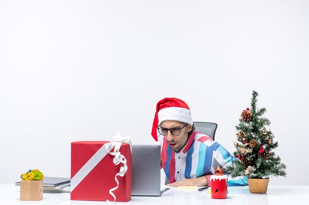 Männlicher Arbeiter der Vorderansicht, der an seinem Platz mit Laptop und Akten sitzt, die Weihnachtsfeiertagsbürojob arbeiten