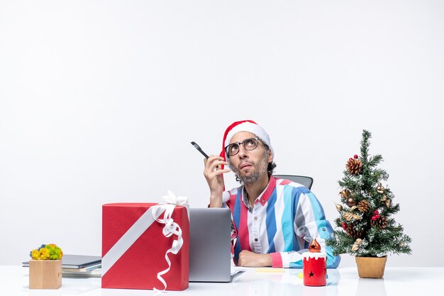 Männlicher Arbeiter der Vorderansicht, der an seinem Platz mit Laptop und Akten sitzt, die Weihnachtsfeiertagsbürojobfarbe arbeiten