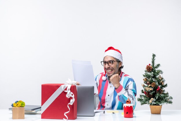 Männlicher Arbeiter der Vorderansicht, der an seinem Platz sitzt, mit Laptop, der Dokumente liest