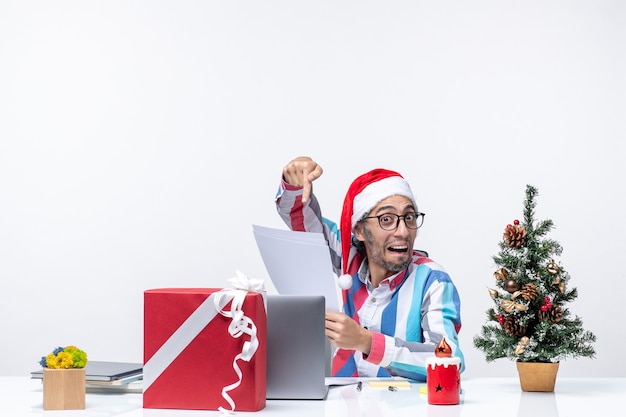 Männlicher Arbeiter der Vorderansicht, der an seinem Platz sitzt, mit Laptop, der Dokumente liest