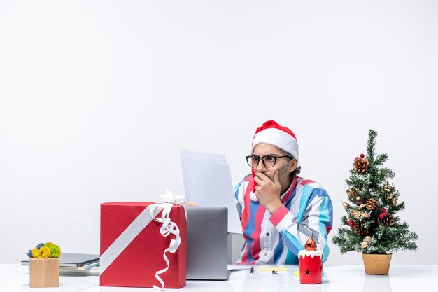 Männlicher Arbeiter der Vorderansicht, der an seinem Platz sitzt, mit Laptop, der Dokumente liest