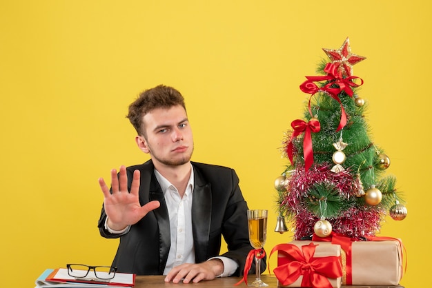 Männlicher Arbeiter der Vorderansicht, der hinter seinem Arbeitsplatz auf Gelb sitzt