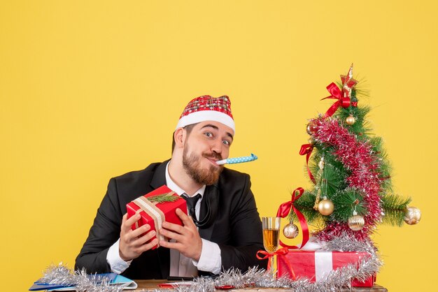 Männlicher Arbeiter der Vorderansicht, der hinter seinem Tisch mit Geschenken auf einem gelben sitzt