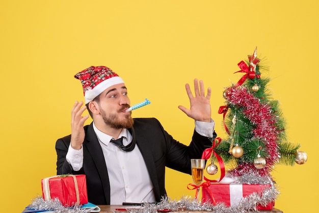 Männlicher Arbeiter der Vorderansicht, der hinter seinem Tisch mit Geschenken auf einem gelben sitzt