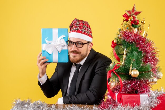 Männlicher Arbeiter der Vorderansicht, der um Weihnachtsgeschenke auf Gelb sitzt