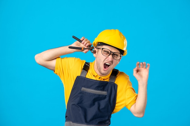 Männlicher Arbeiter der Vorderansicht in Uniform, die sein Ohr mit einer Zange auf Blau schneidet