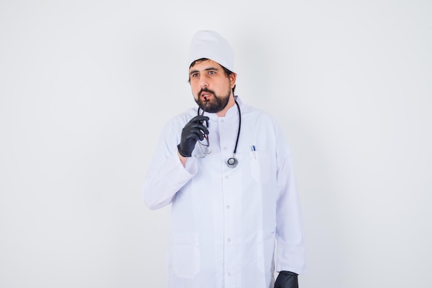 Männlicher Arzt beißt Gläser in weißer Uniform und sieht fokussiert aus. Vorderansicht.