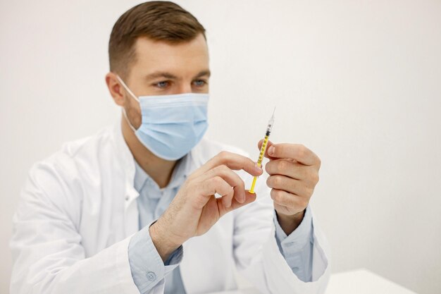 Männlicher Arzt, der eine Spritze hält, während er isoliert auf weißem Hintergrund sitzt