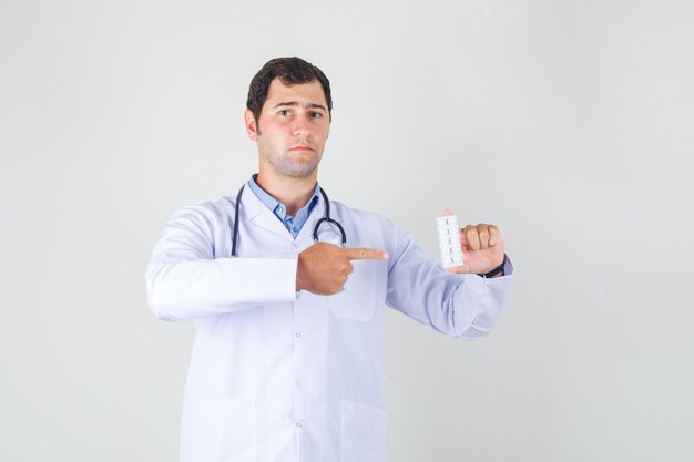 Männlicher Arzt, der Finger auf Pillen im weißen Kittel zeigt und ernst schaut. Vorderansicht.