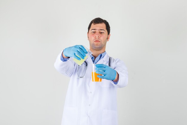 Männlicher Arzt, der Fruchtsaft durch Eingießen in weißen Kittel, Handschuhe mischt