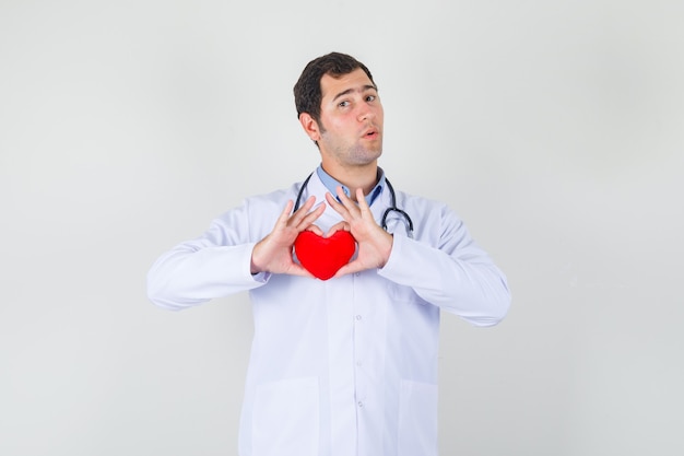Männlicher Arzt, der rotes Herz im weißen Kittel hält