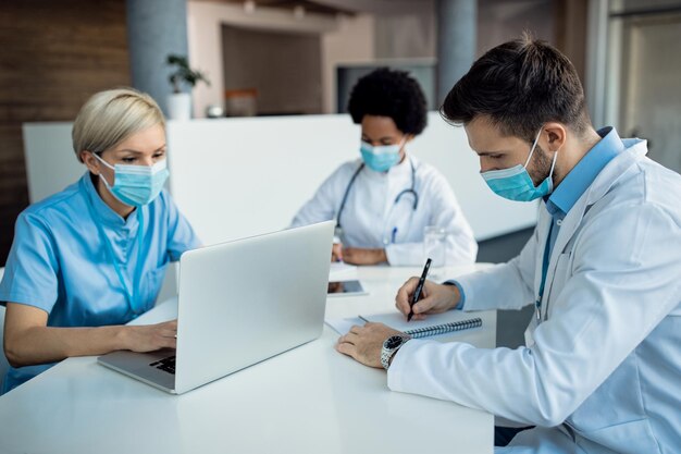 Männlicher Arzt, der sich Notizen macht, während er mit Kollegen in der medizinischen Klinik arbeitet