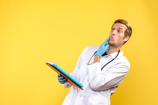 Männlicher Arzt der Vorderansicht, der Analysen auf dem gelben Hintergrundmedizinvirusgesundheitsmensch hält