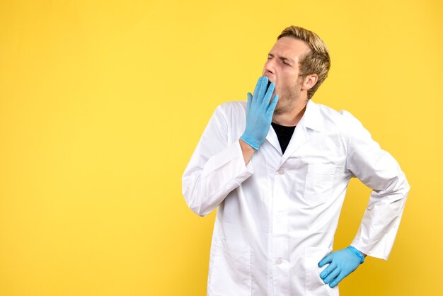 Männlicher Arzt der Vorderansicht, der auf gelbem Hintergrundmediziner-menschliche Pandemie-Covid gähnt