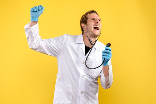 Männlicher Arzt der Vorderansicht, der auf gelbem Hintergrundvirus-Gesundheitsemotionsmediziner schreit