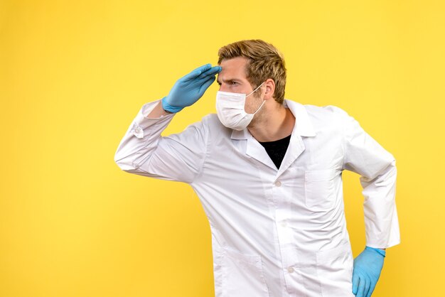 Männlicher Arzt der Vorderansicht, der Entfernung auf Pandemie-Covid-Gesundheitsmediziner des gelben Hintergrunds betrachtet