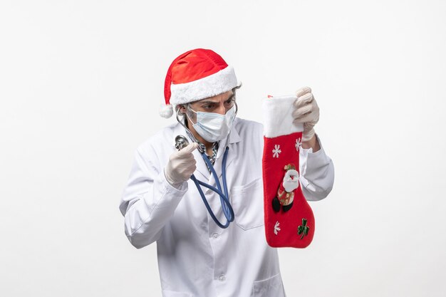 Männlicher Arzt der Vorderansicht, der Feiertagssocke an Feiertagen des weißen Wand-Covid-Virus beobachtet