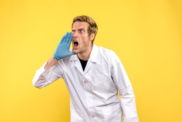 Männlicher Arzt der Vorderansicht, der laut auf gelbe Hintergrundmedizinergesundheits-Covid-Pandemie anruft