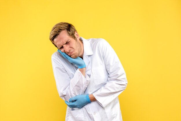 Männlicher Arzt der Vorderansicht, der Zahnschmerzen auf menschlichem Pandemie-Covid des gelben Hintergrundmediziners hat