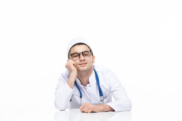 Männlicher Arzt der Vorderansicht im medizinischen Anzug, der hinter Schreibtisch sitzt