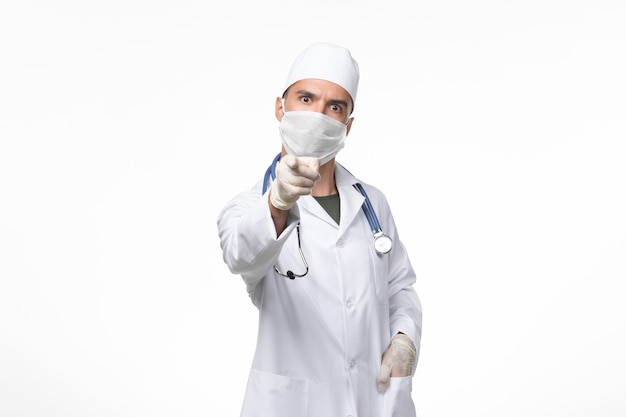 Männlicher Arzt der Vorderansicht im medizinischen Anzug und Tragen einer Maske gegen Covid, die auf das Pandemievirus der weißen Wand-Covid-Krankheitskrankheit hinweist