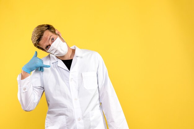 Männlicher Arzt der Vorderansicht in der Maske auf dem gelben Hintergrundgesundheitspandemie-Covid-Virus