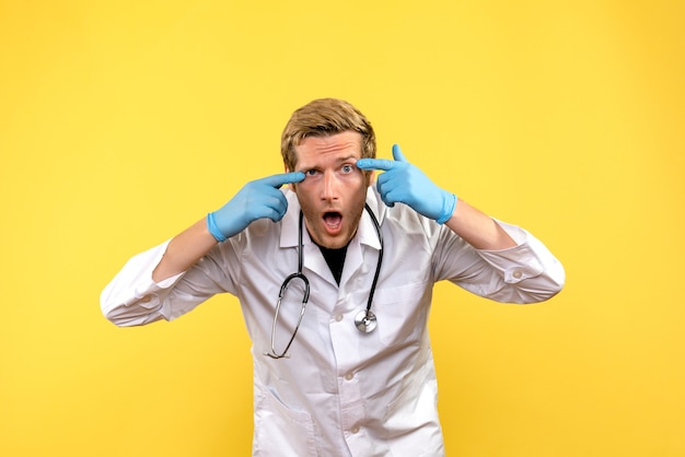 Männlicher Arzt der Vorderansicht überrascht auf menschlichem Virus des gelben Hintergrundgesundheitsarztes