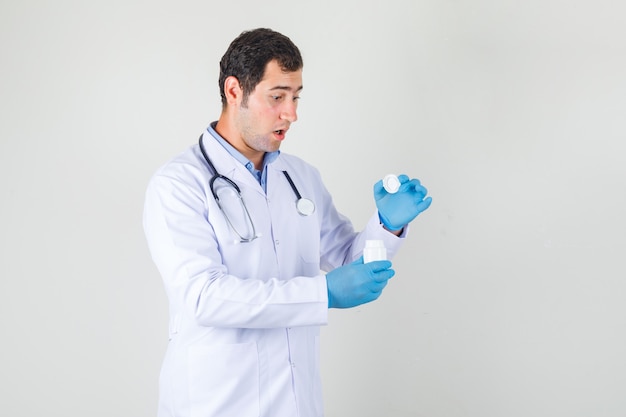 Männlicher Arzt im weißen Kittel, Handschuhe, die Flasche Pillen öffnen und schockiert schauen