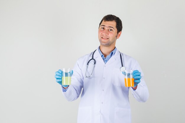 Männlicher Arzt im weißen Kittel, Handschuhe, die Saft in Gläsern halten und fröhlich schauen
