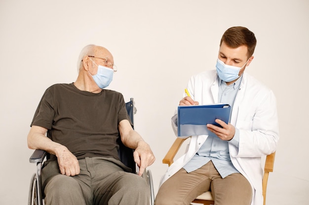 Männlicher Arzt und alter Mann im Rollstuhl isoliert auf weißem Hintergrund