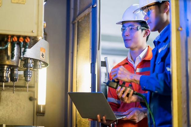 Männlicher asiatischer Ingenieurfachmann, der eine Diskussion im Stehen über eine cnc-Maschine in der Fabrik führt, zwei asiatische Mitarbeiter, die den Prozess der cnc-Betriebsmaschine erklären und lösen