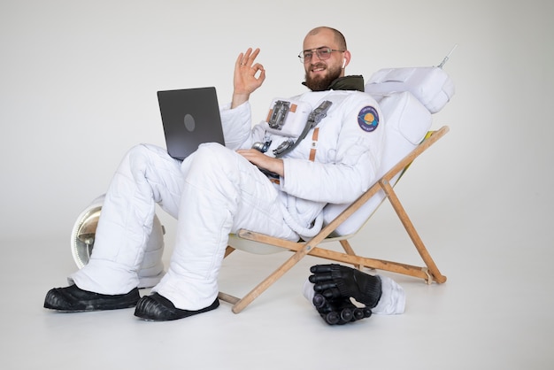 Männlicher Astronaut, der das Okay-Zeichen zeigt, während er am Laptop arbeitet